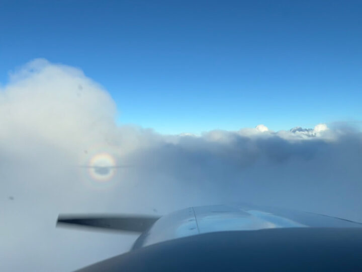Airplane wing above clouds with circular rainbow halo