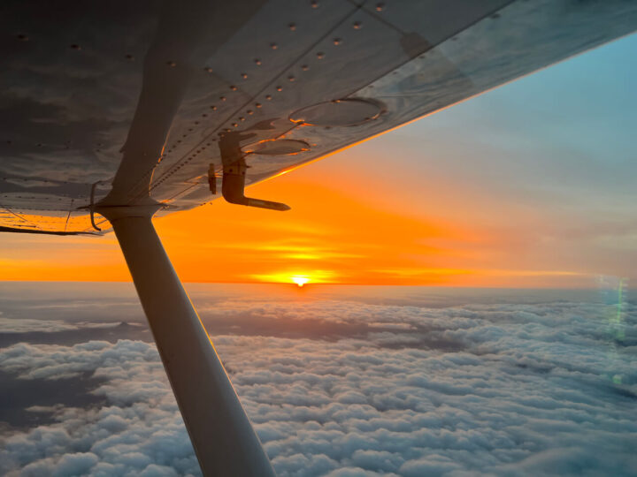 Airplane wing above clouds at sunset